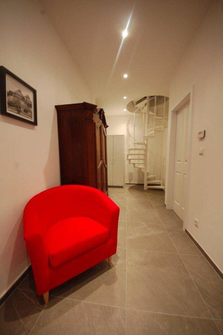 Flur mit einem auffälligen roten Sessel und einer eleganten Wendeltreppe.
