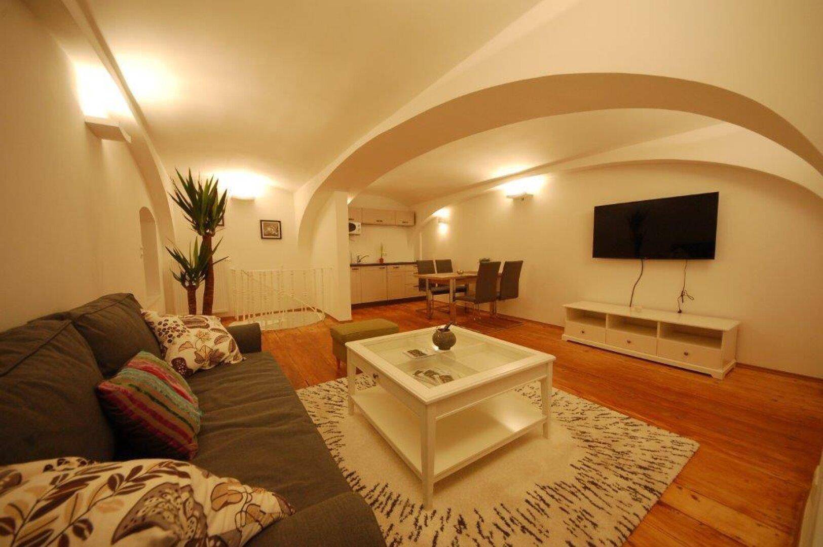 Geräumiger Wohn- und Essbereich mit Sofa, Fernseher und integrierter Küchenzeile.