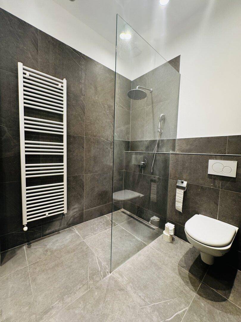 Modernes Badezimmer mit begehbarer Dusche, Wand-WC und beheiztem Handtuchhalter.