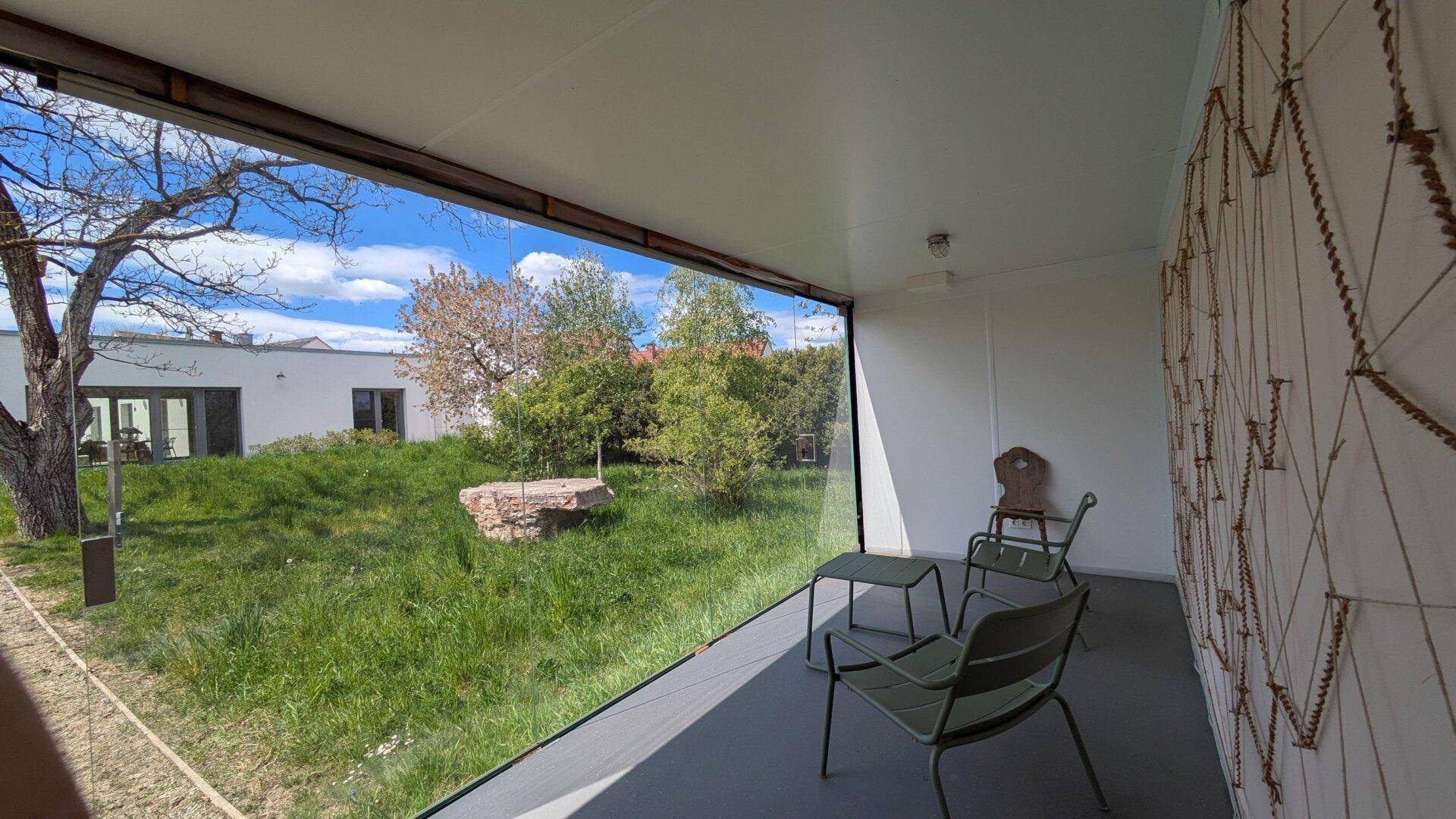 Überdachte Loggia mit Glaswänden und Blick auf den grünen Garten und die umliegende Natur.