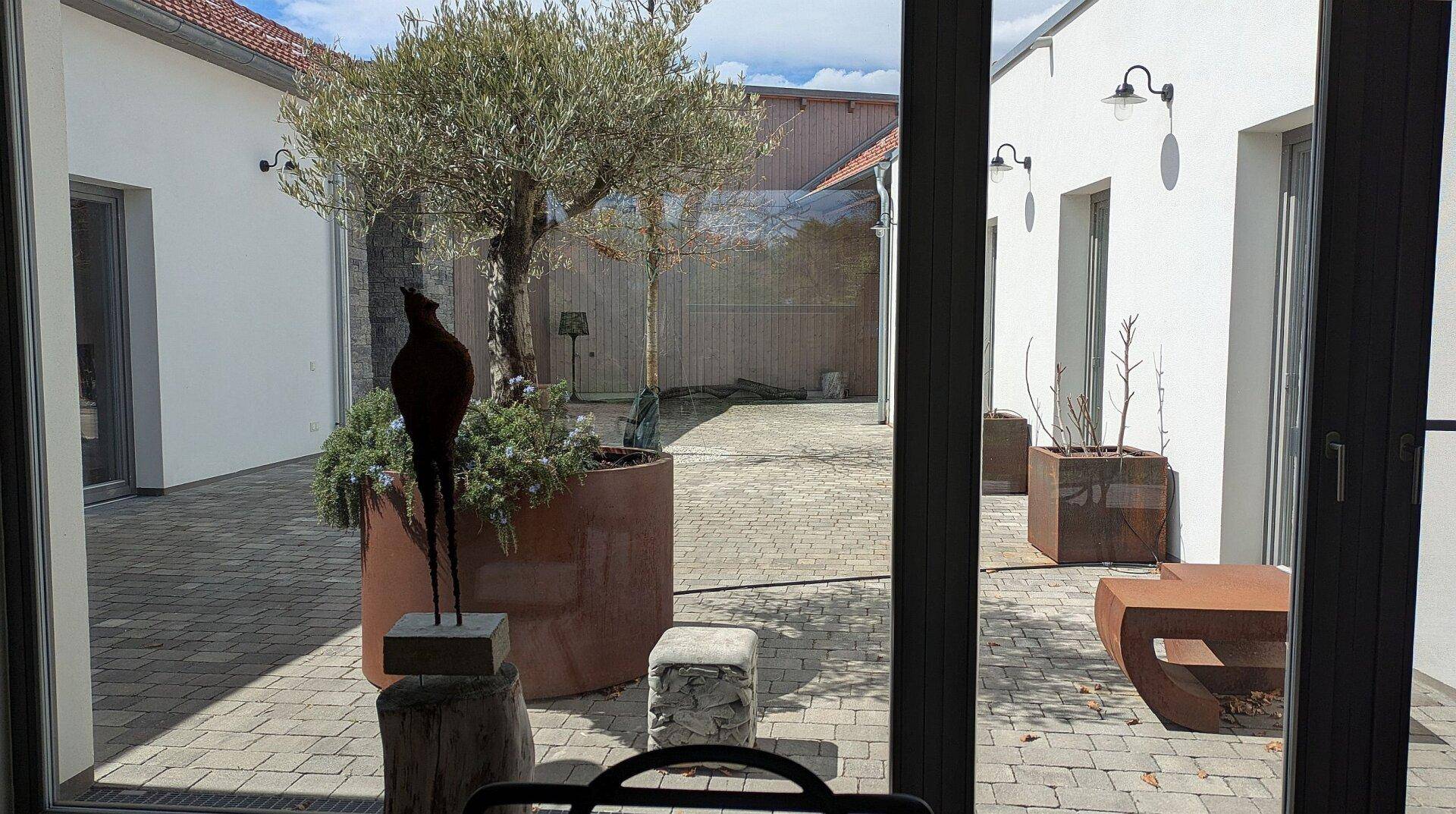 Blick aus dem Fenster auf einen gepflasterten Innenhof mit dekorativen Pflanzen und Skulpturen.