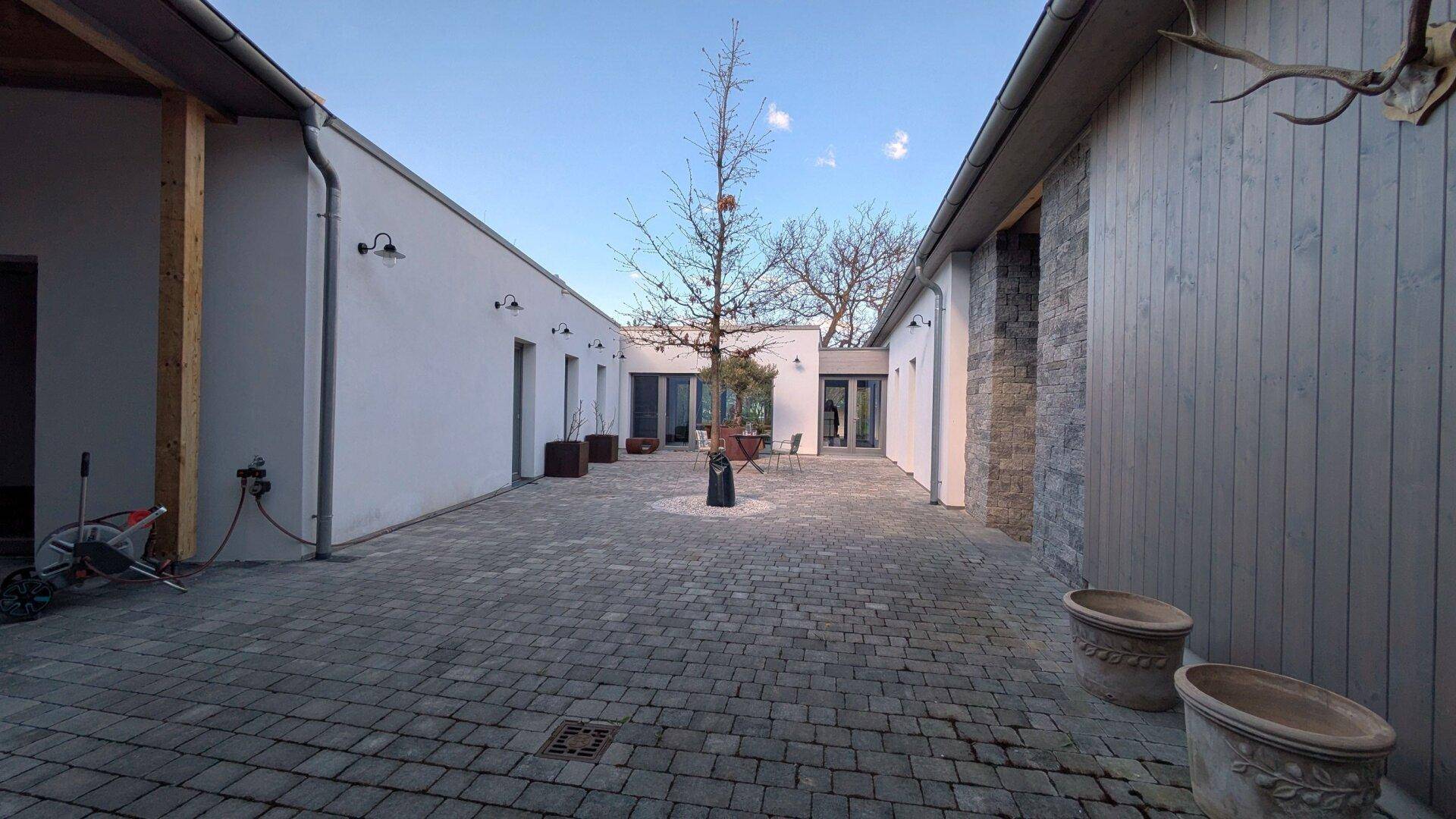 Großer gepflasterter Innenhof mit einem Baum in der Mitte, umgeben von modernen Gebäuden.