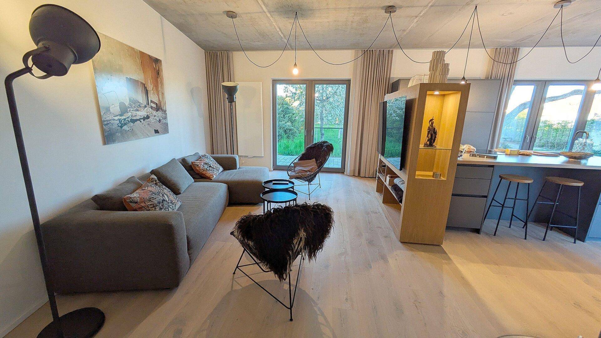 Heller Wohnbereich mit großem Sofa, Holzboden und offener Verbindung zur Küche.