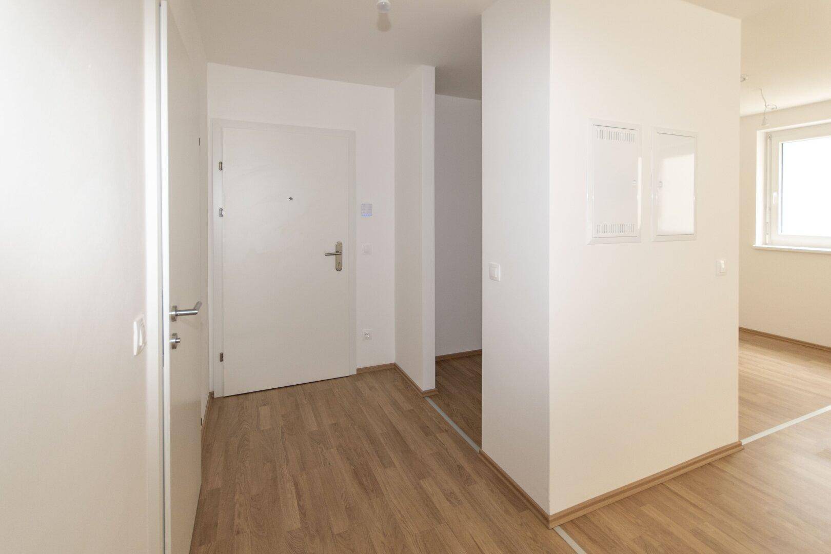 Eingangsbereich mit weißer Wohnungstür, hellem Laminatboden und Zugang zu weiteren Räumen.