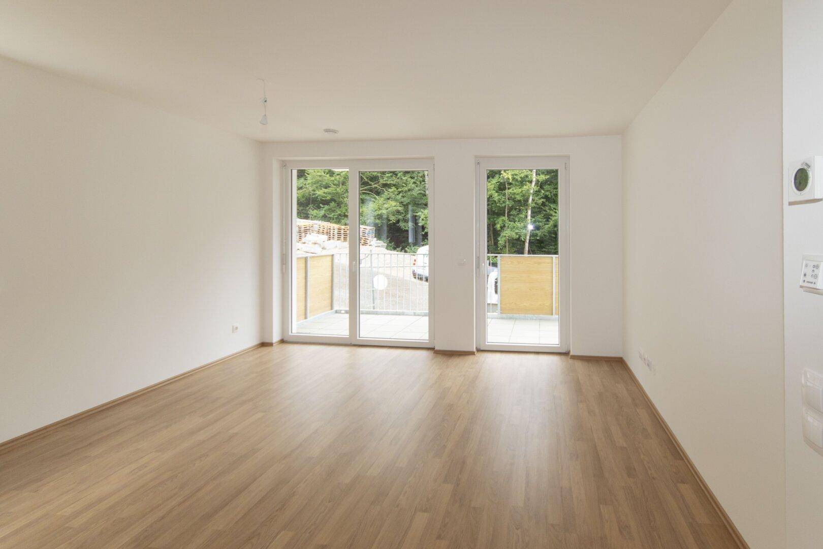 Helles Wohnzimmer mit Laminatboden und großen Schiebetüren, die auf einen Balkon führen.
