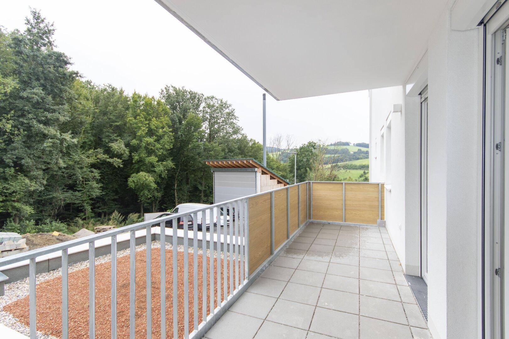 Geräumiger Balkon mit Fliesenboden und Holzsichtschutz, bietet einen weiten Blick ins Grüne.