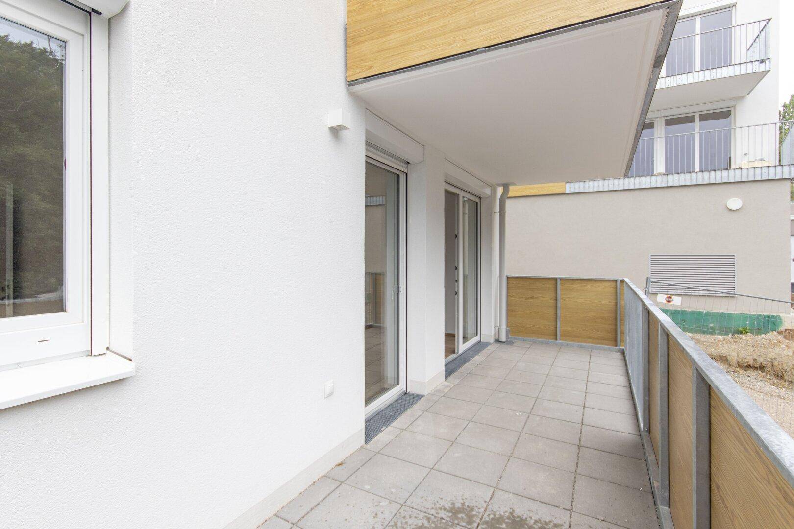 Balkon mit Fliesenboden und Holzsichtschutz, zugänglich durch große Glasschiebetüren.