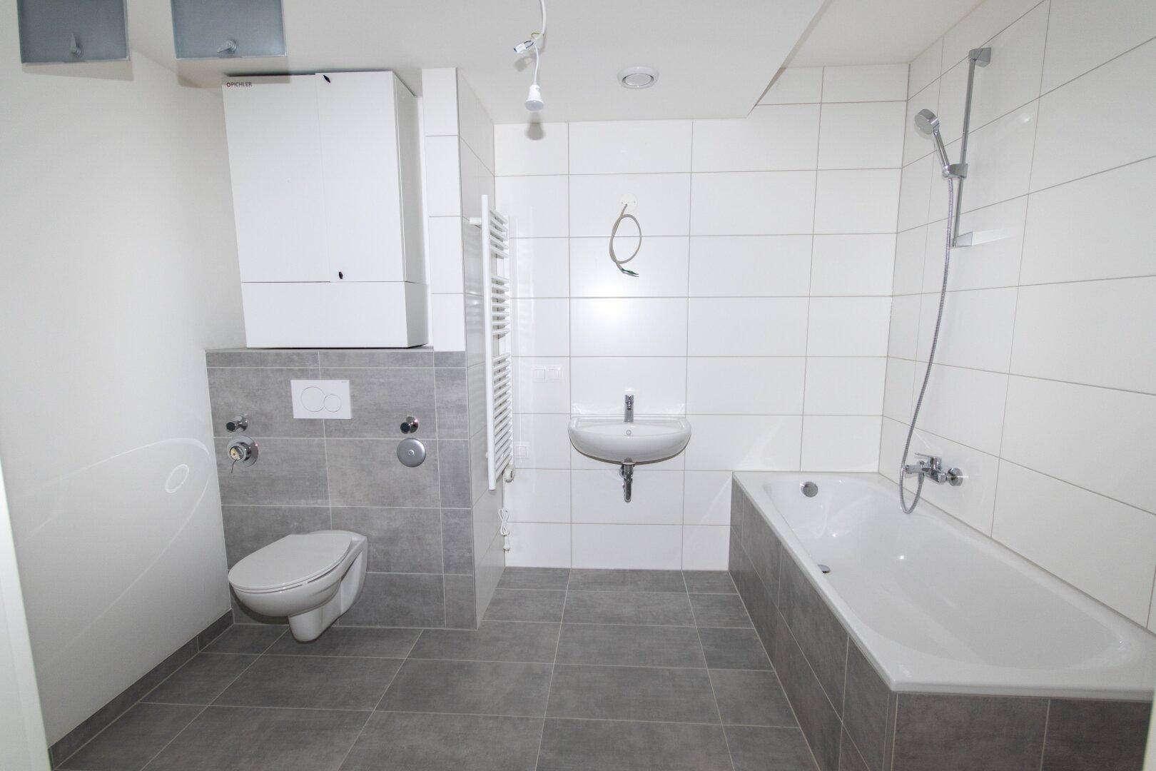 Modernes Badezimmer mit grauen Bodenfliesen, weißer Wandverkleidung, Badewanne und Hänge-WC.