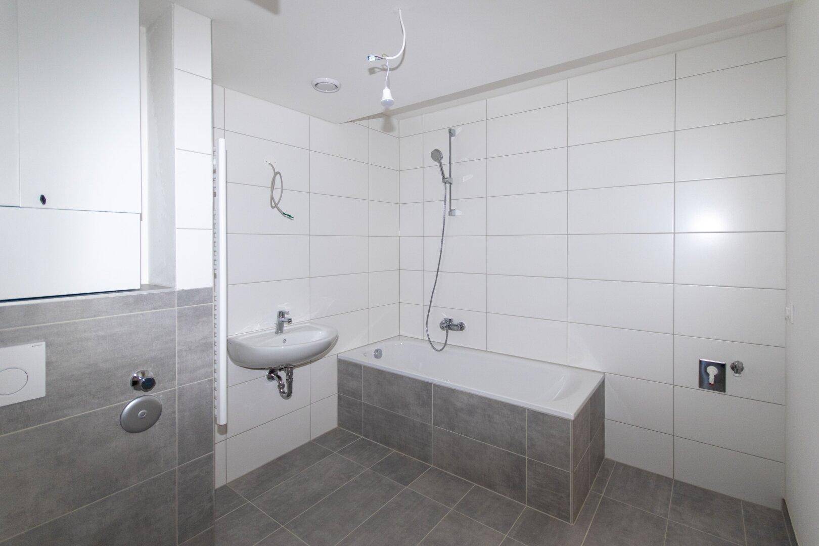 Funktionales Badezimmer mit grauen Bodenfliesen, weißer Wandverkleidung und Badewanne.