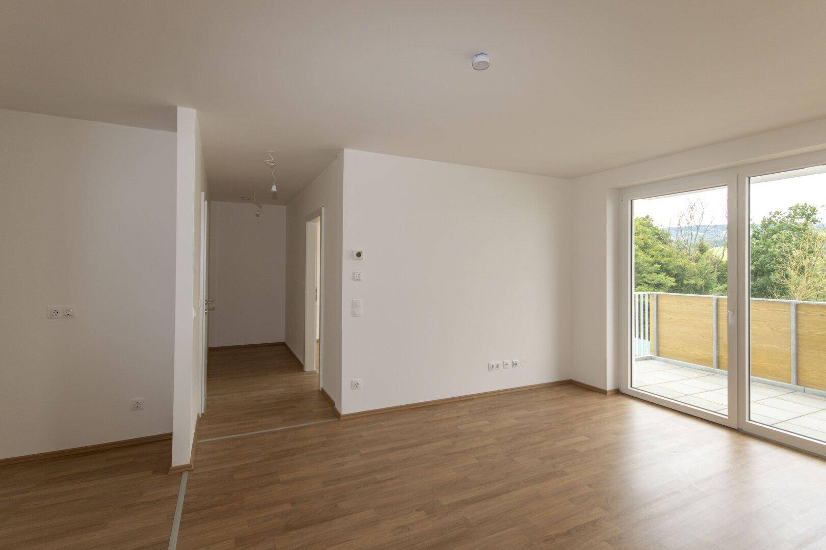 Helles Wohnzimmer mit Laminatboden und offenem Übergang zum Flurbereich.
