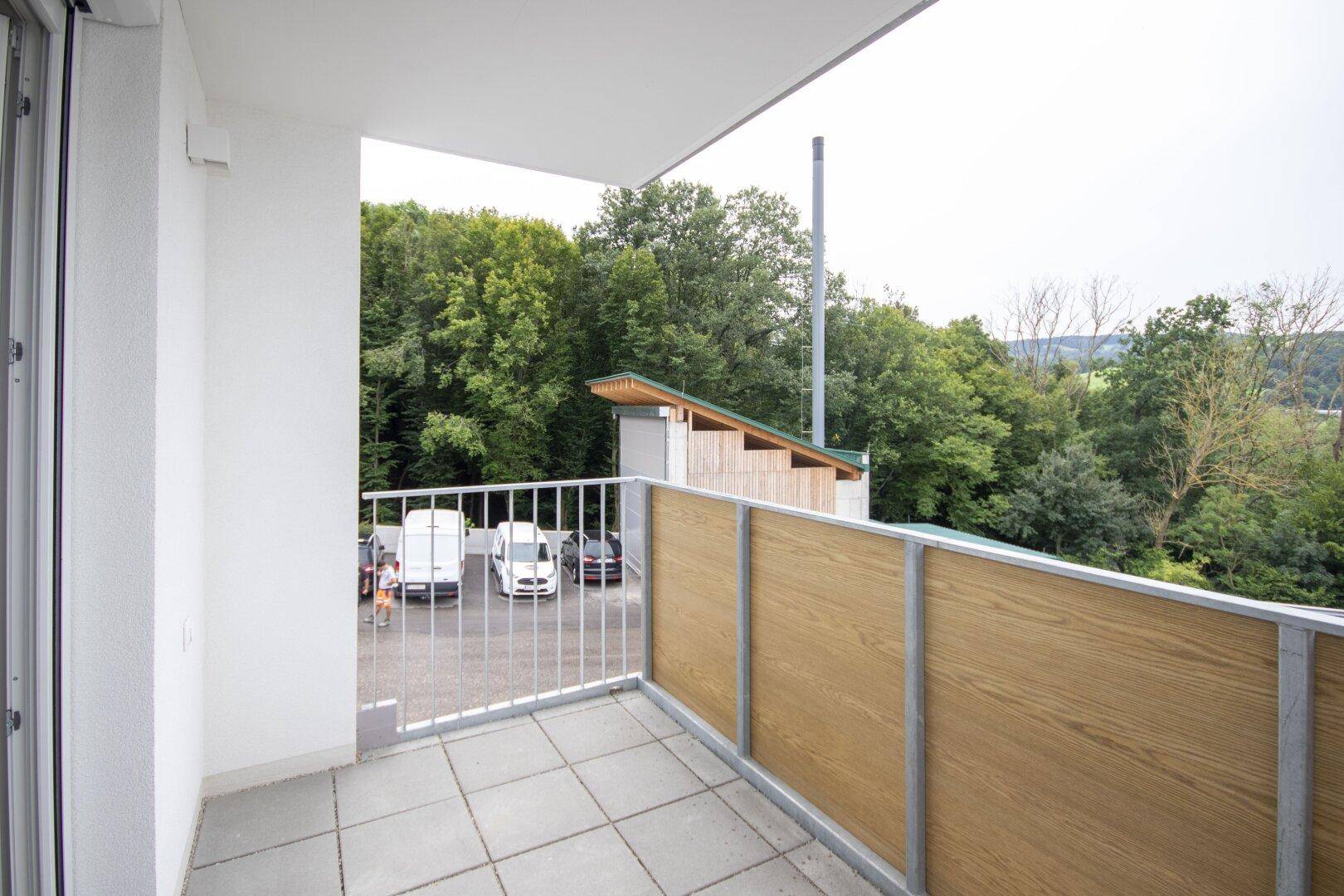 Balkon mit Fliesenboden, Holzsichtschutz und Blick auf Bäume und Parkplätze.