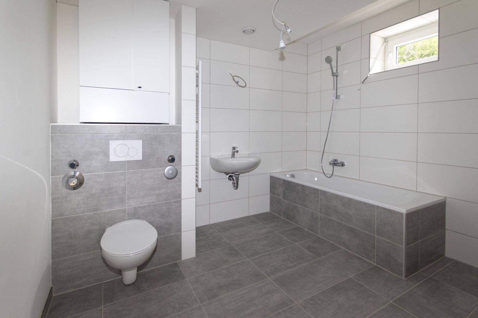 Modernes Badezimmer mit grauen Bodenfliesen, weißer Wandverkleidung und Badewanne.