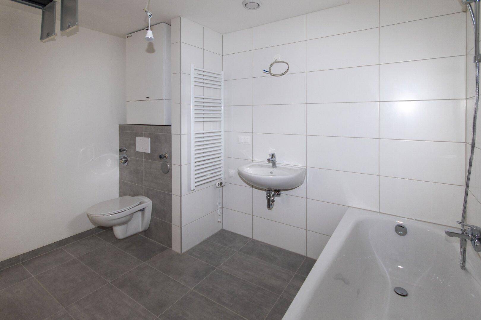 Modernes Badezimmer mit Badewanne, Wand-WC und beheiztem Handtuchhalter.