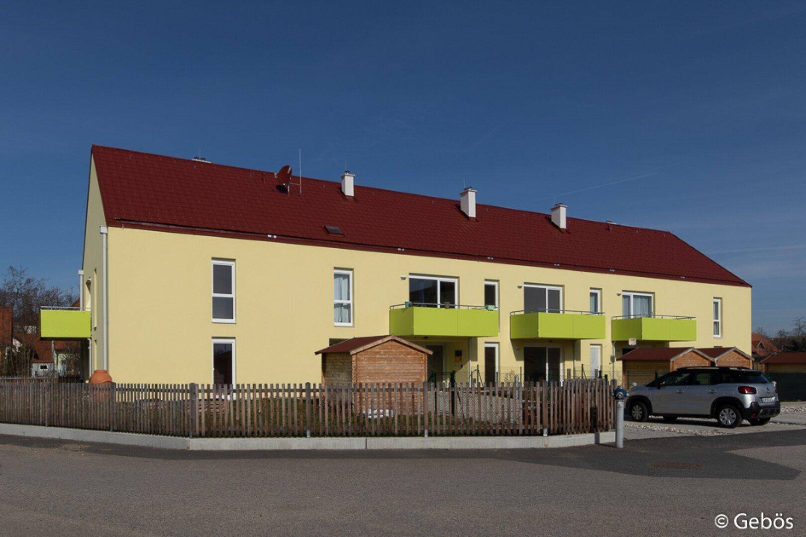 Ansicht eines modernen Wohnhauses mit gelber Fassade, rotem Dach und Balkonen.