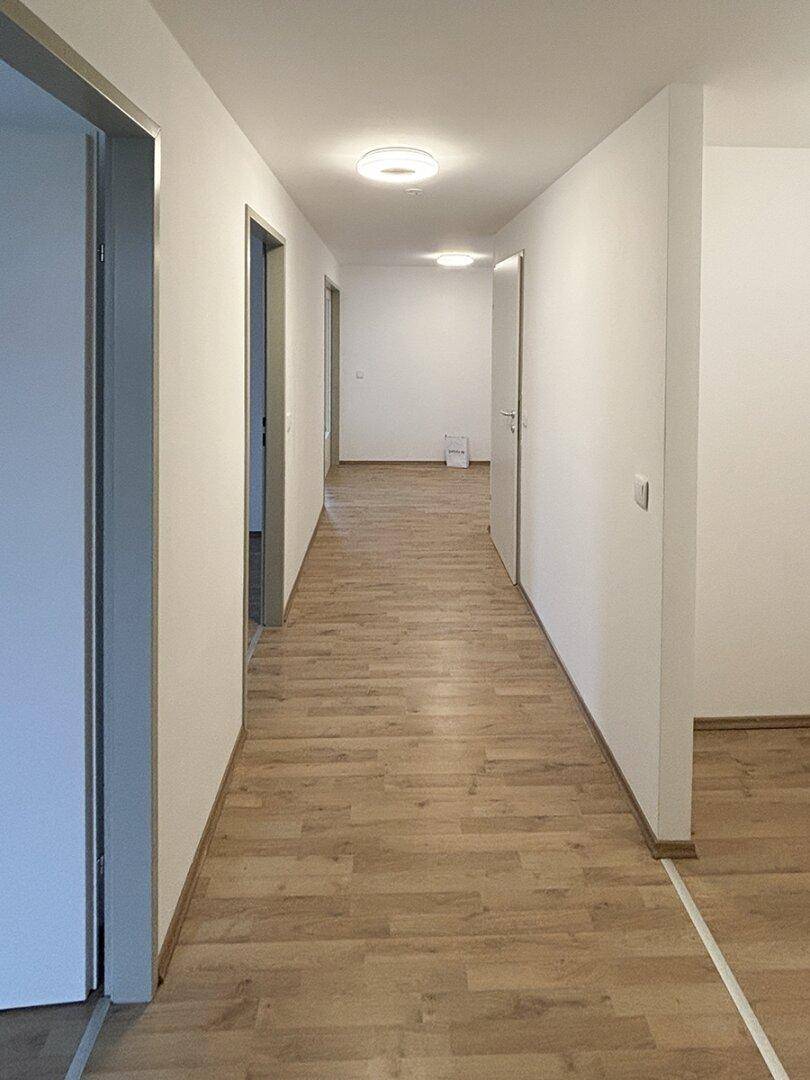 Langer, heller Flur mit Laminatboden und weißen Wänden, der zu weiteren Zimmern führt.