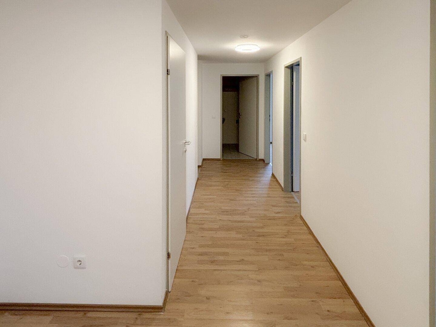 Heller Flur mit Laminatboden und mehreren Türen, der verschiedene Räume miteinander verbindet.