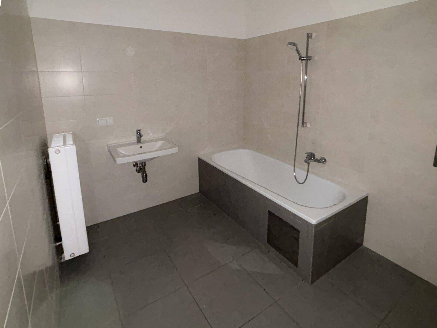 Badezimmer mit Badewanne, Waschbecken und Fliesen an Wänden und Boden.