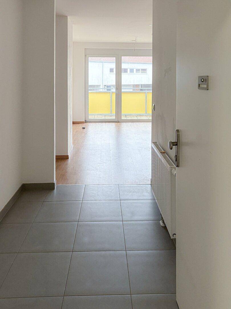 Heller Eingangsbereich mit Fliesenboden, der zu einem Raum mit Balkonzugang führt.