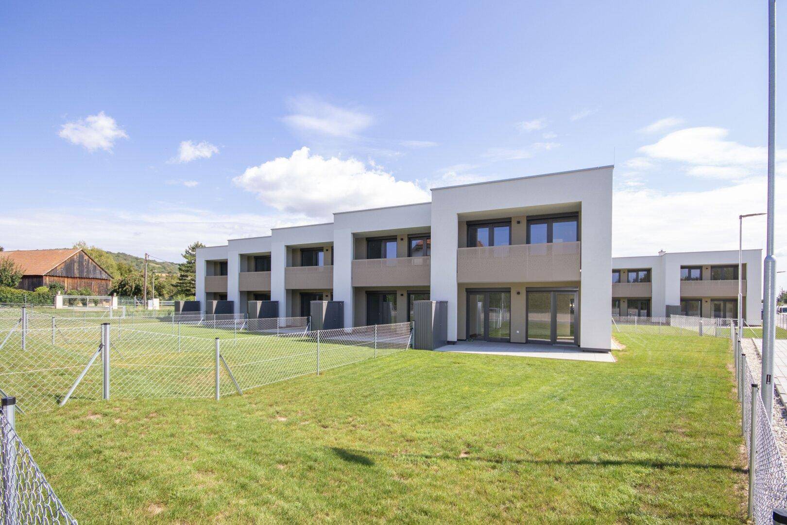 Moderne Reihenhäuser mit weißer Fassade, großen Fenstern und grüner Rasenfläche.