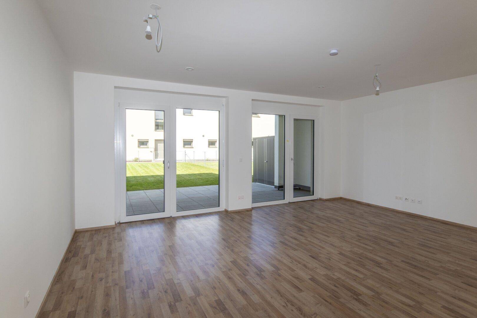Heller Wohnraum mit Holzboden und großen Glastüren, die zum Garten führen.
