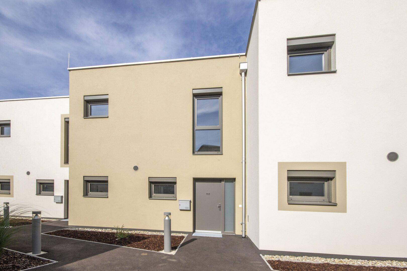 Moderner Eingangsbereich eines Reihenhauses mit beigefarbener Fassade und kleinen Fenstern.