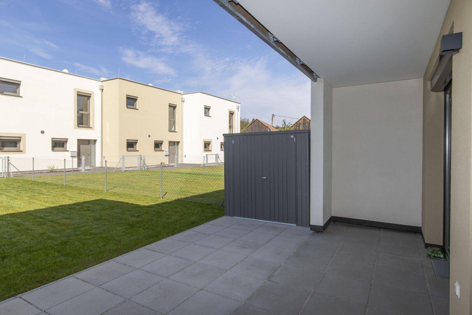 Gepflasterte Terrasse mit Blick auf den Rasen und einen praktischen Gartenschuppen.