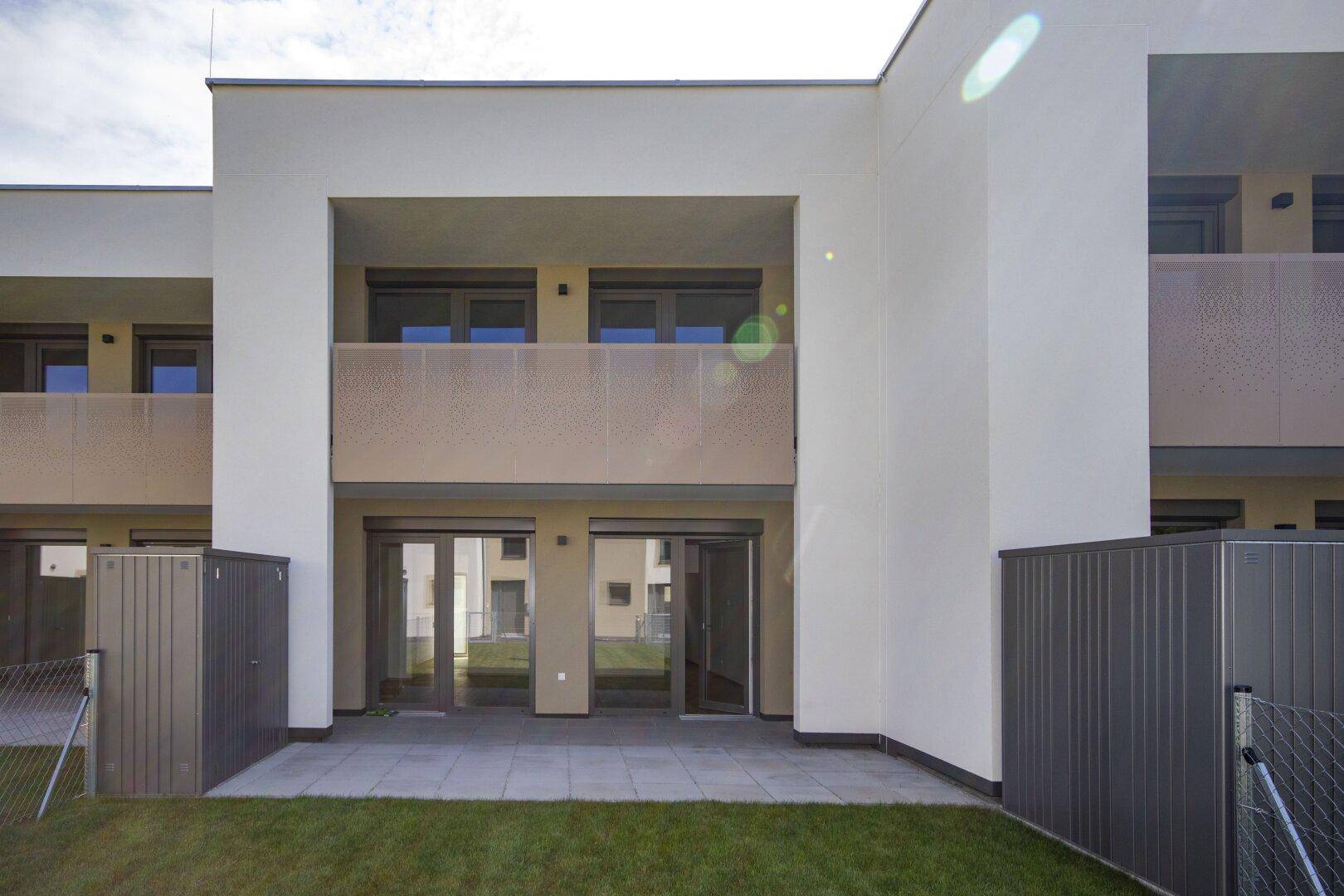 Rückseite des Gebäudes mit einer ebenerdigen Terrasse und einem darüberliegenden Balkon.