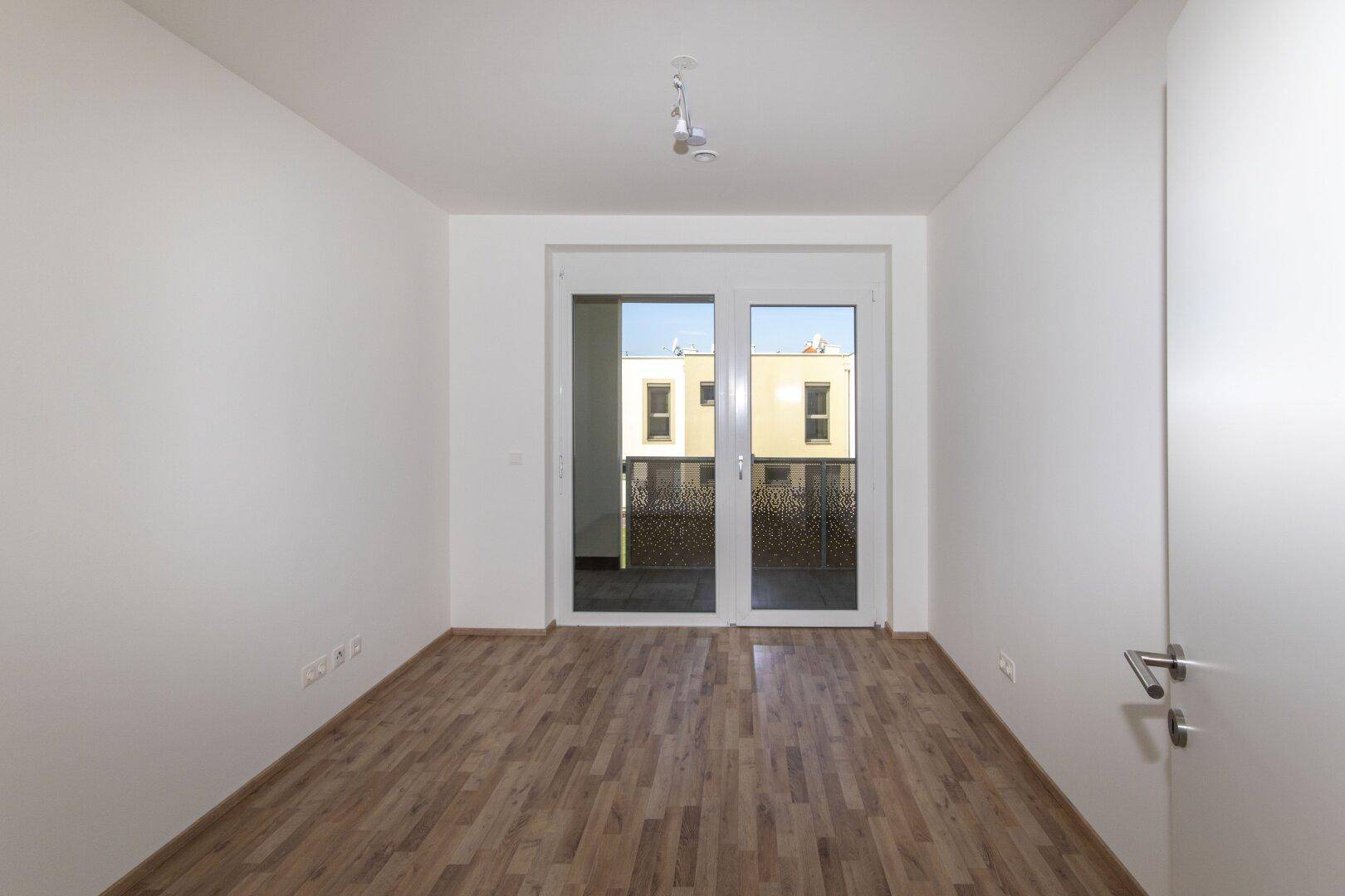 Helles Schlafzimmer mit Holzboden und direktem Zugang zu einem Balkon.