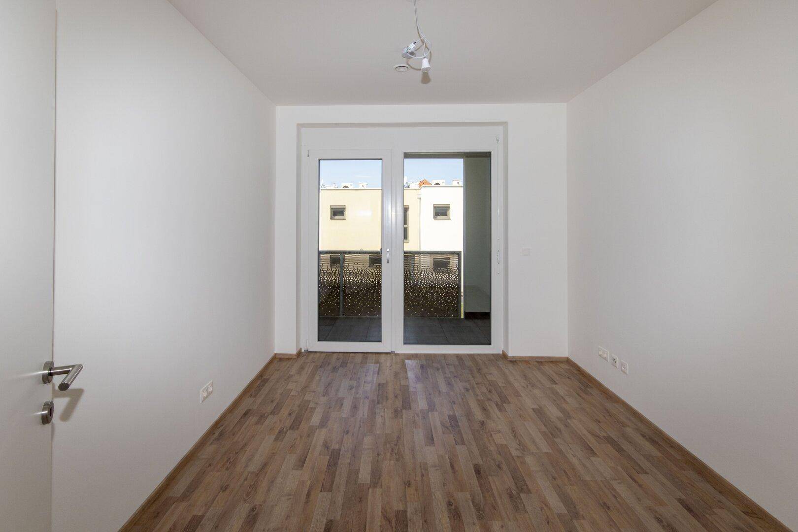 Geräumiges Schlafzimmer mit Holzboden und großen Fenstern, die auf einen Balkon führen.