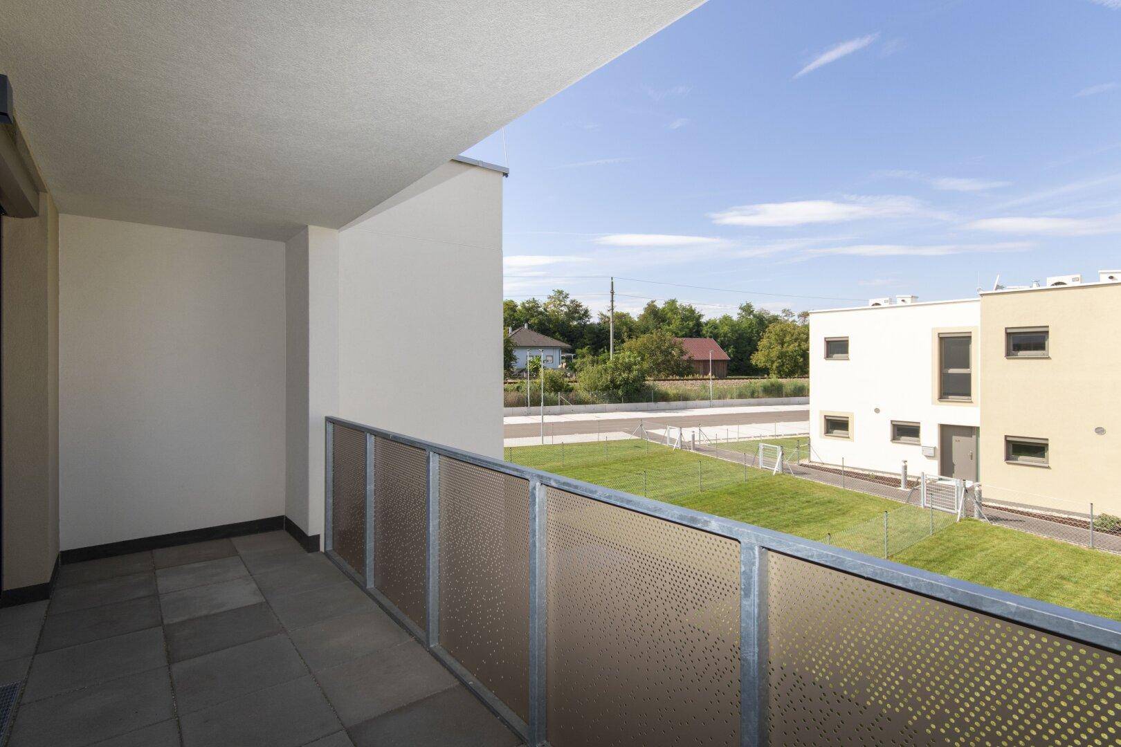 Geräumiger Balkon mit Fliesenboden und Blick auf die umliegende Landschaft und Nachbarhäuser.