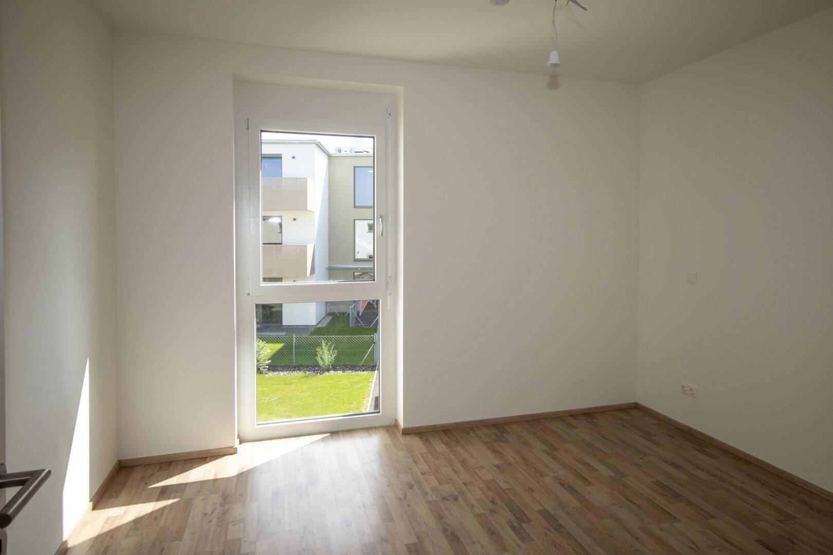 Helles Zimmer mit großem Fenster und Blick auf den grünen Gartenbereich.