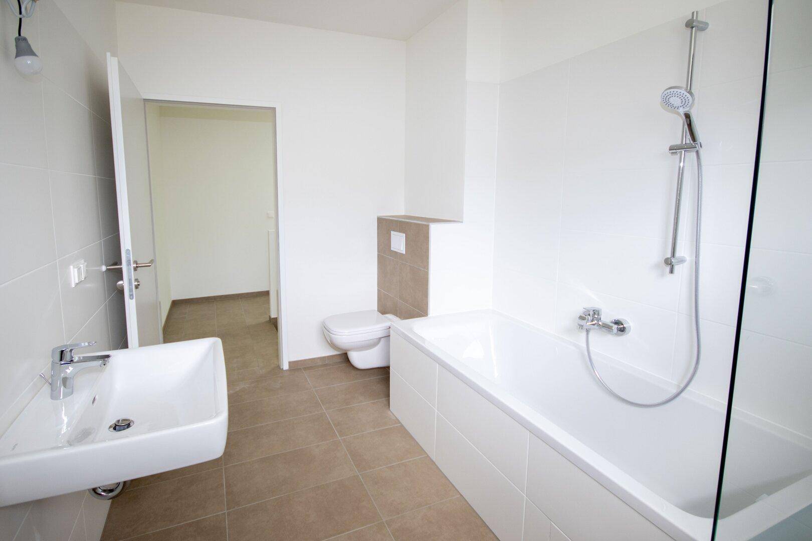 Modernes Badezimmer mit Badewanne, Dusche, WC und Waschbecken, hell gefliest.