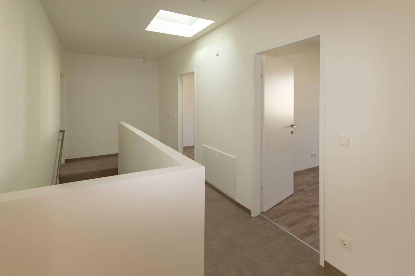 Heller Flur im Obergeschoss mit natürlichem Licht durch ein Dachfenster und Fliesenboden.