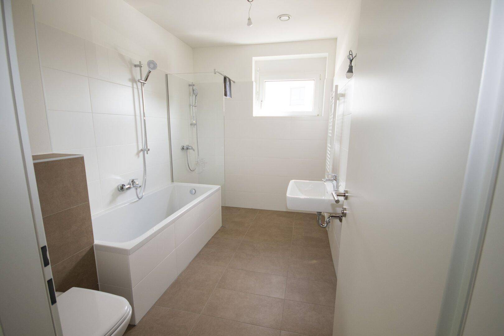 Helles Badezimmer mit Badewanne, Dusche und Fenster, ausgestattet mit modernen Armaturen.
