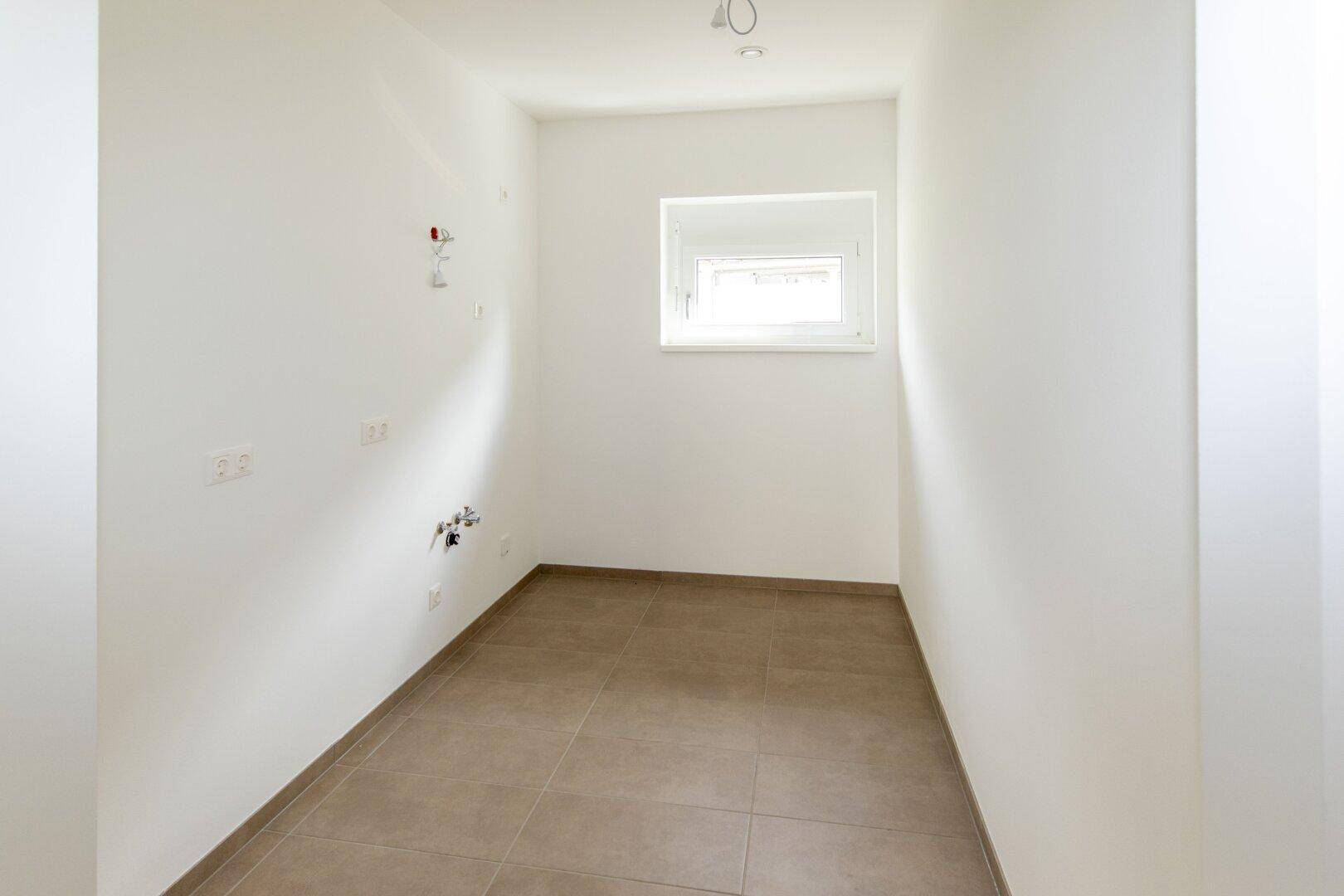 Kleiner Hauswirtschaftsraum mit Fenster und hellbraunen Fliesen, ideal für Lagerung.