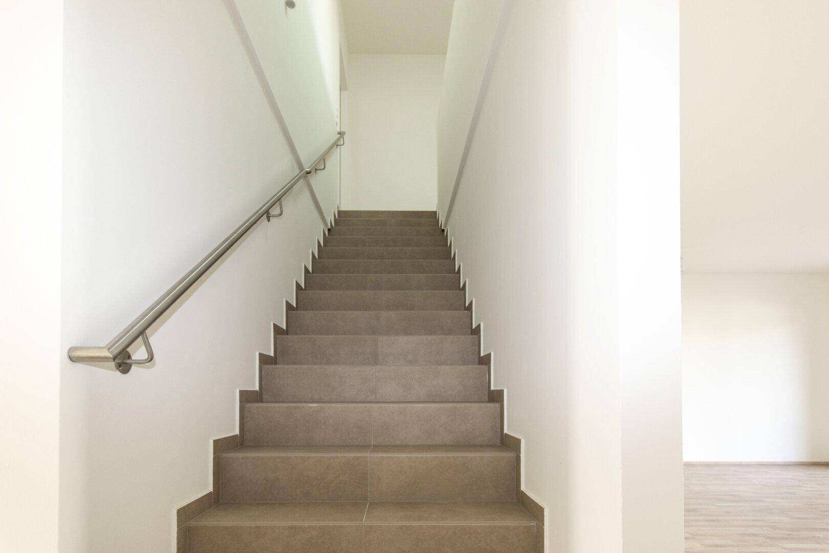 Treppenhaus mit gefliesten Stufen und modernem Edelstahlgeländer, das in die obere Etage führt.