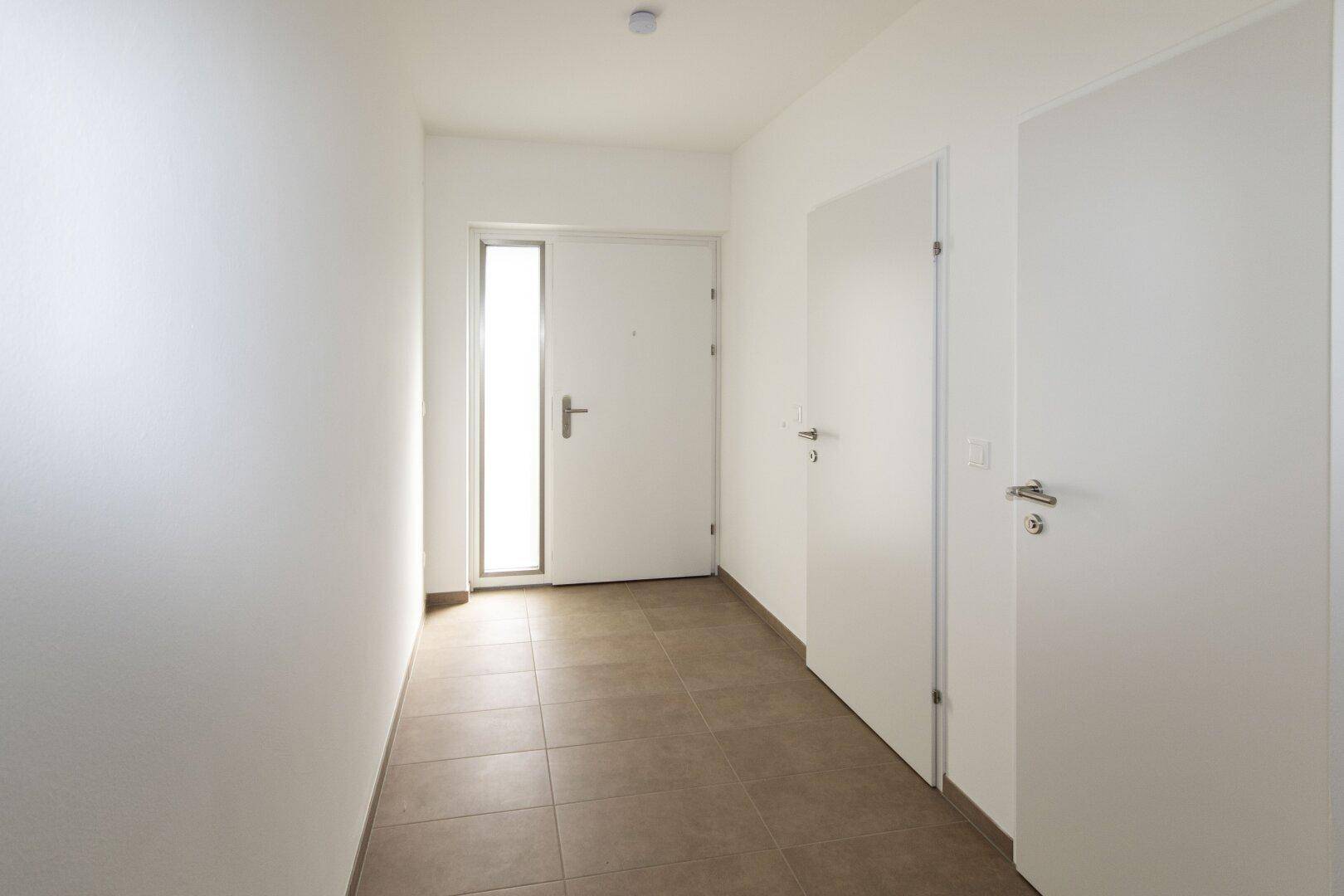 Eingangsbereich mit Fliesenboden und heller Tür mit Glaseinsatz, die viel Licht hereinlässt.