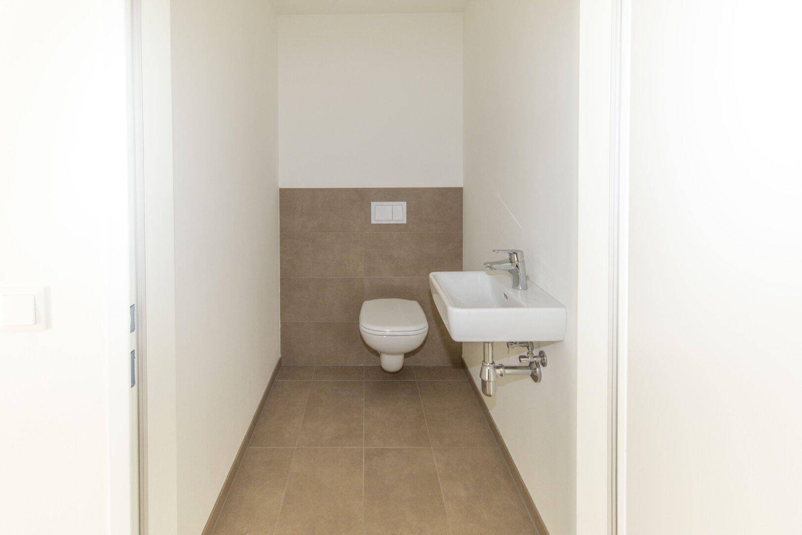 Modernes Gäste-WC mit Wand-WC und kleinem Waschbecken, hell gefliest.