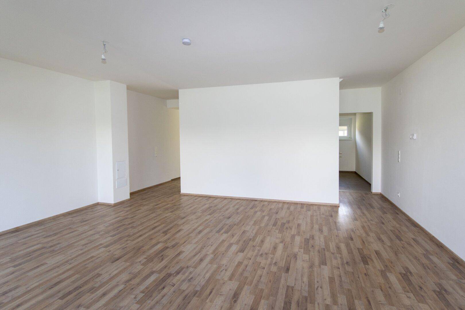 Geräumiger, heller Wohnbereich mit Holzboden und weiß gestrichenen Wänden.