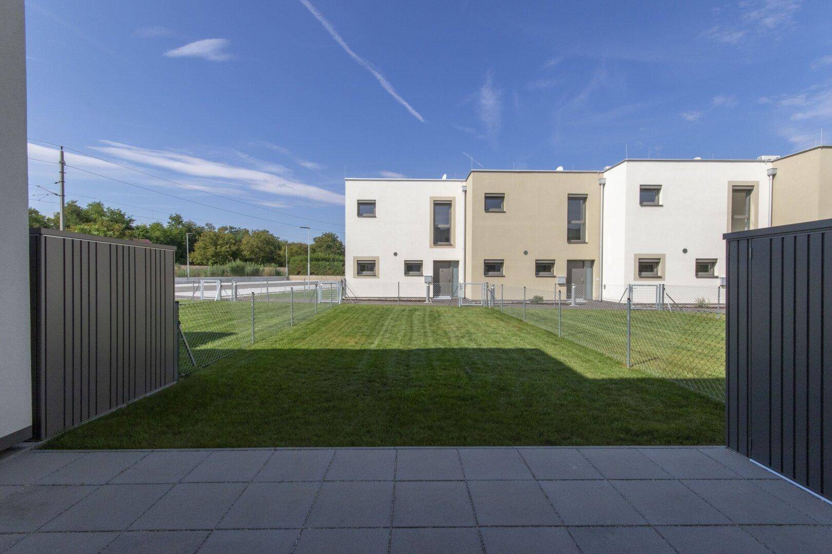 Gepflasterte Terrasse mit Rasenfläche und Blick auf die modernen Reihenhäuser.