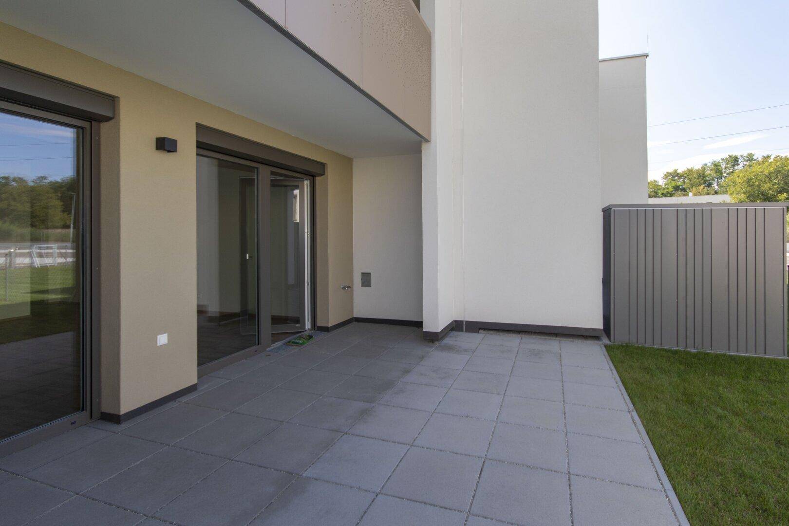 Breite Terrasse mit Schiebetüren zum Innenbereich und angrenzender Rasenfläche.