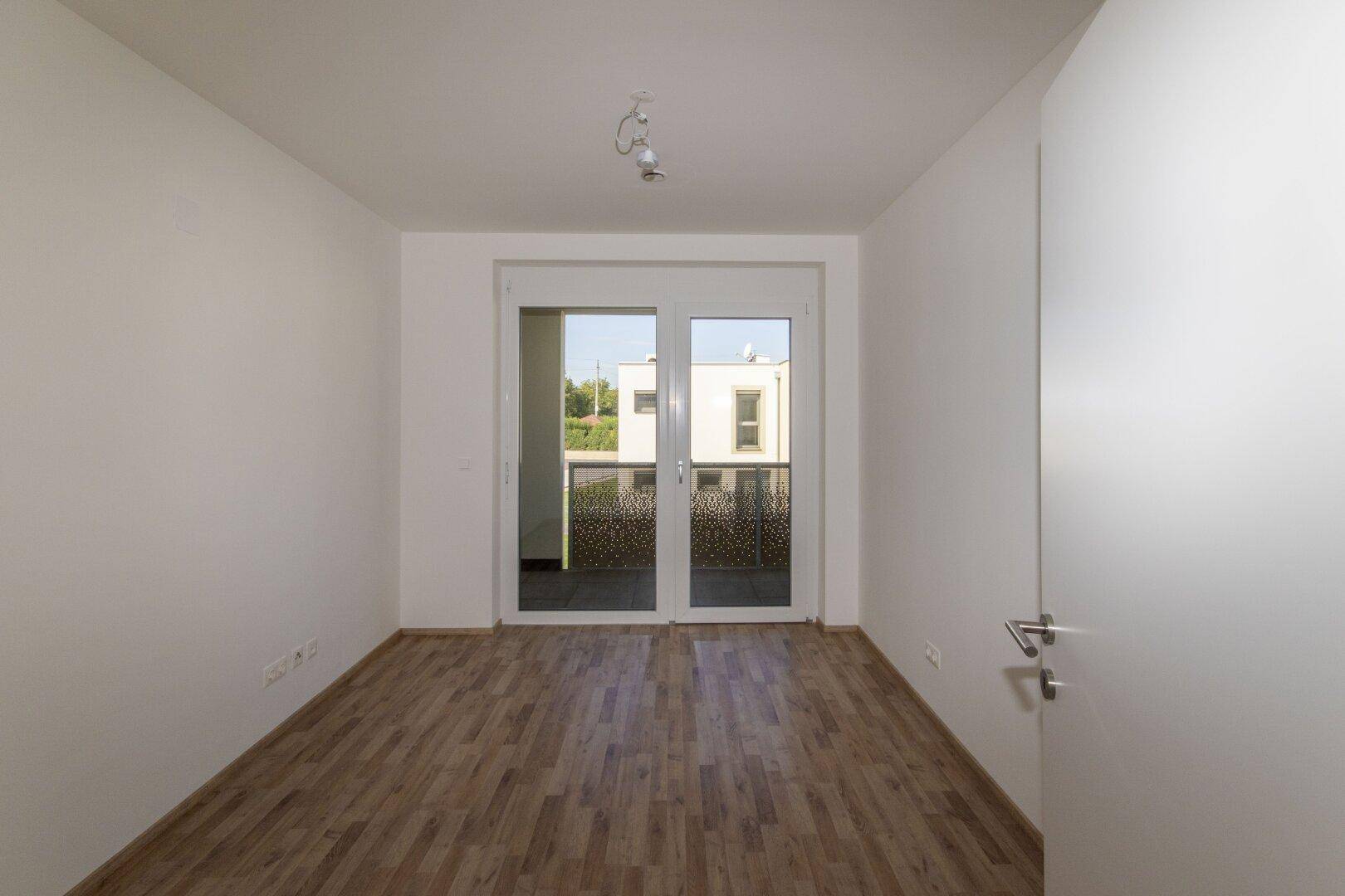 Helles Zimmer mit Holzboden und Zugang zu einem Balkon, ideal als Schlafzimmer.