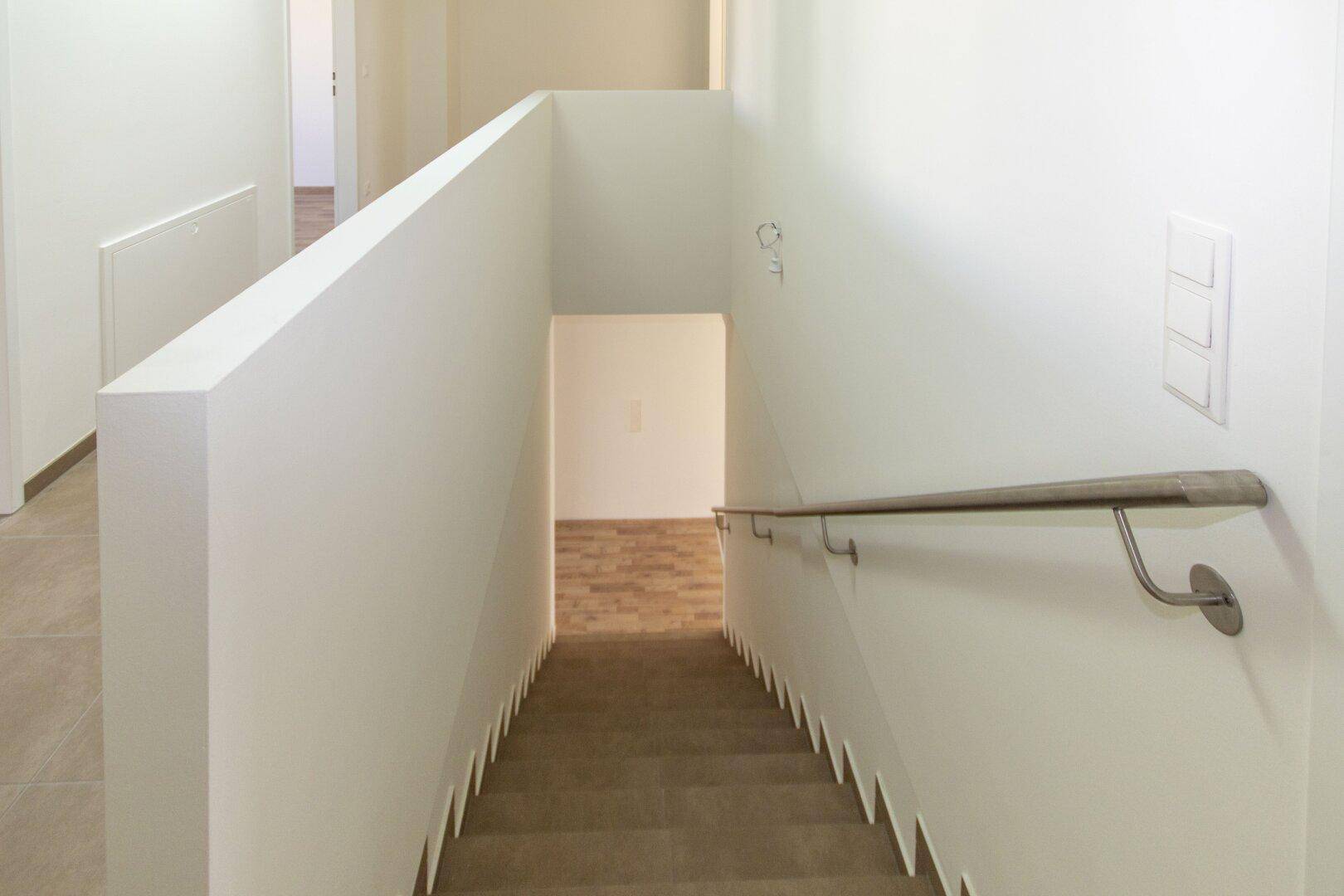 Treppenabgang mit Holzstufen und schlichtem Geländer, führt in den unteren Bereich.