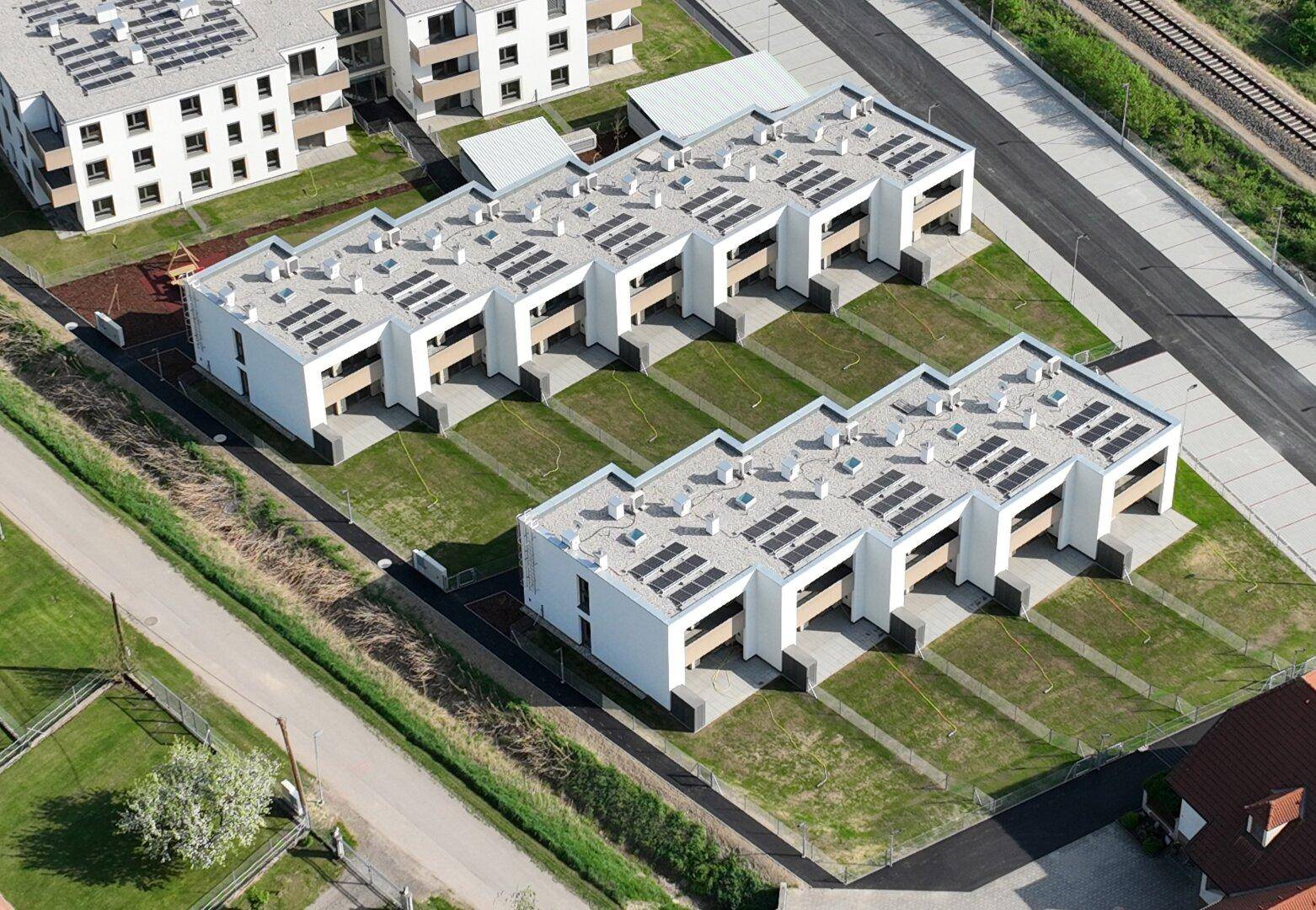 Luftaufnahme einer Wohnanlage mit modernen Gebäuden, Flachdächern und Photovoltaikanlagen.