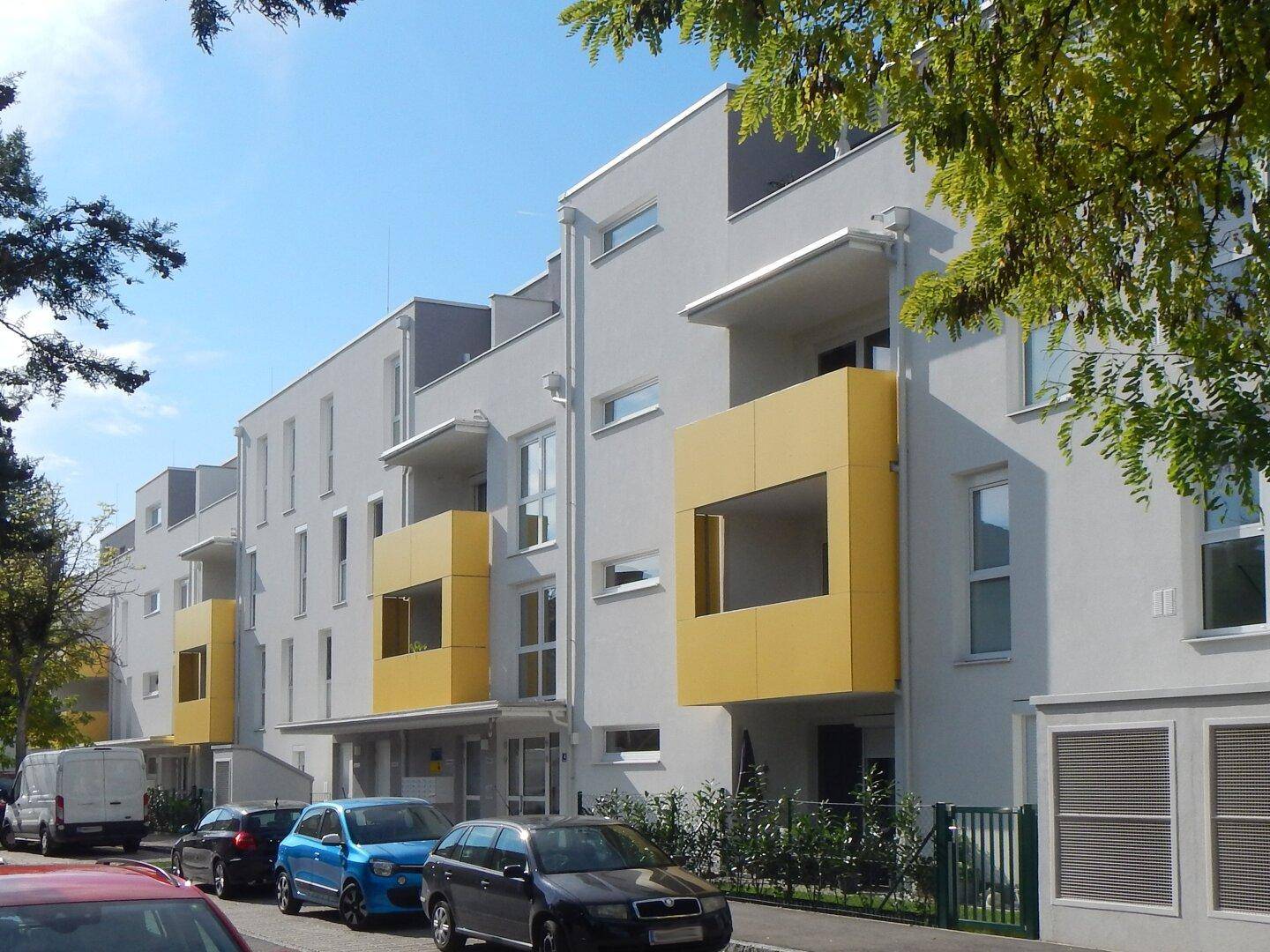 Moderne Wohngebäude mit gelben Balkonen und großen Fenstern entlang einer Straße.