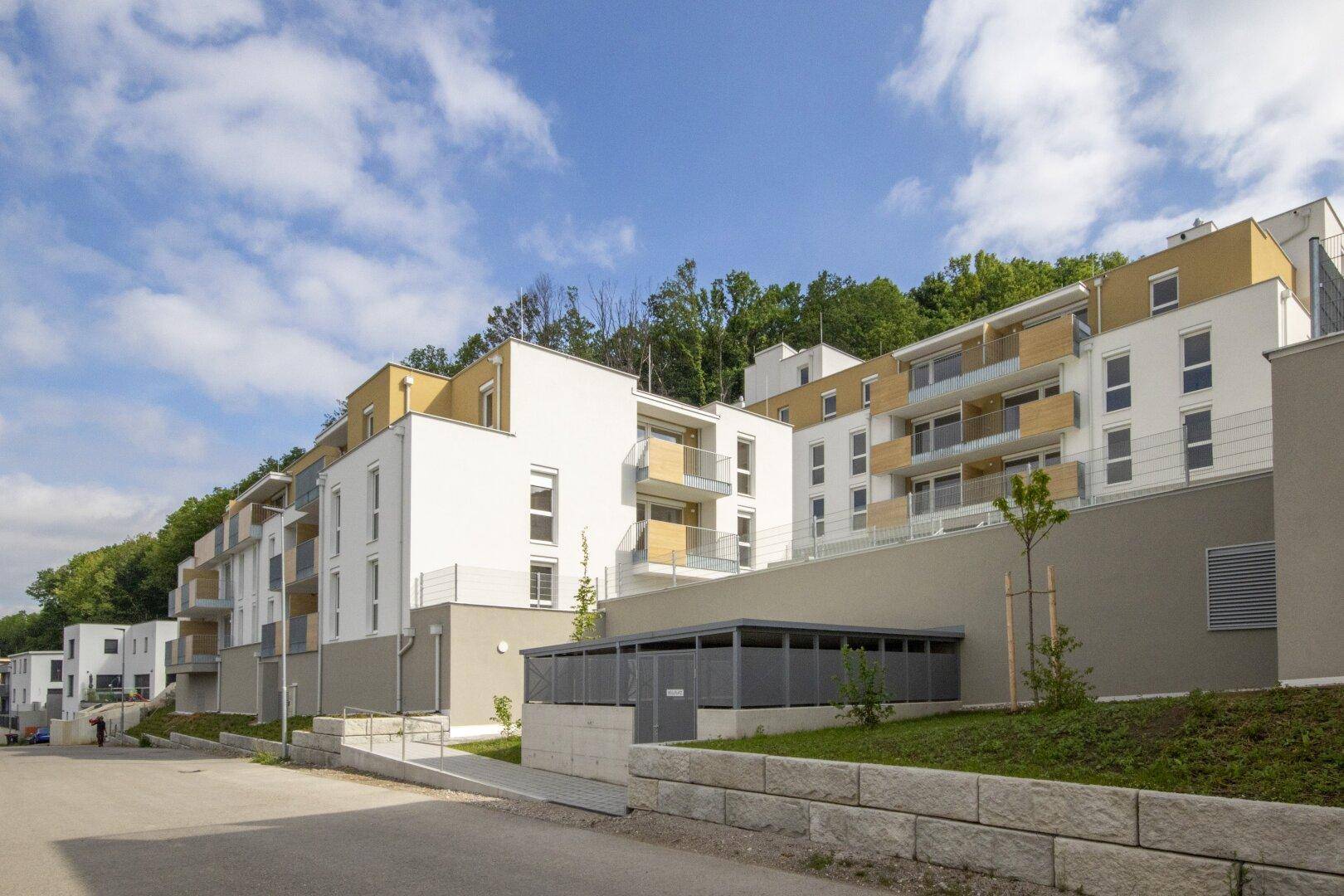 Reihen moderner Wohngebäude in Hanglage, umgeben von viel Grün und Bäumen.