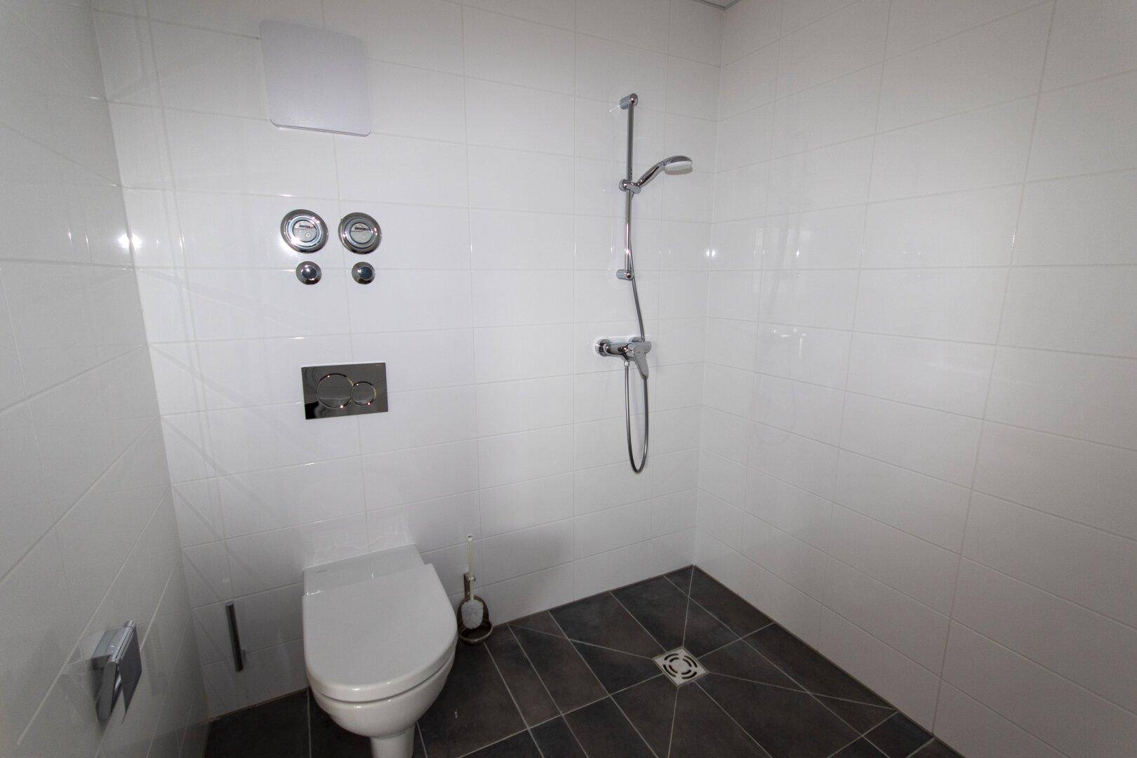 Modernes Badezimmer mit weiß gefliesten Wänden, wandhängendem WC und ebenerdiger Dusche.