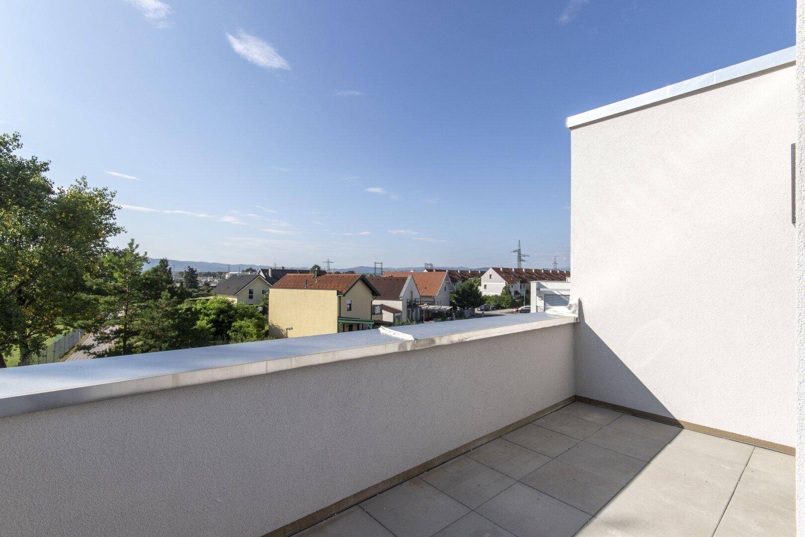 Sonniger Balkon mit Fliesenboden und weitem Blick über die umliegende Wohnsiedlung.