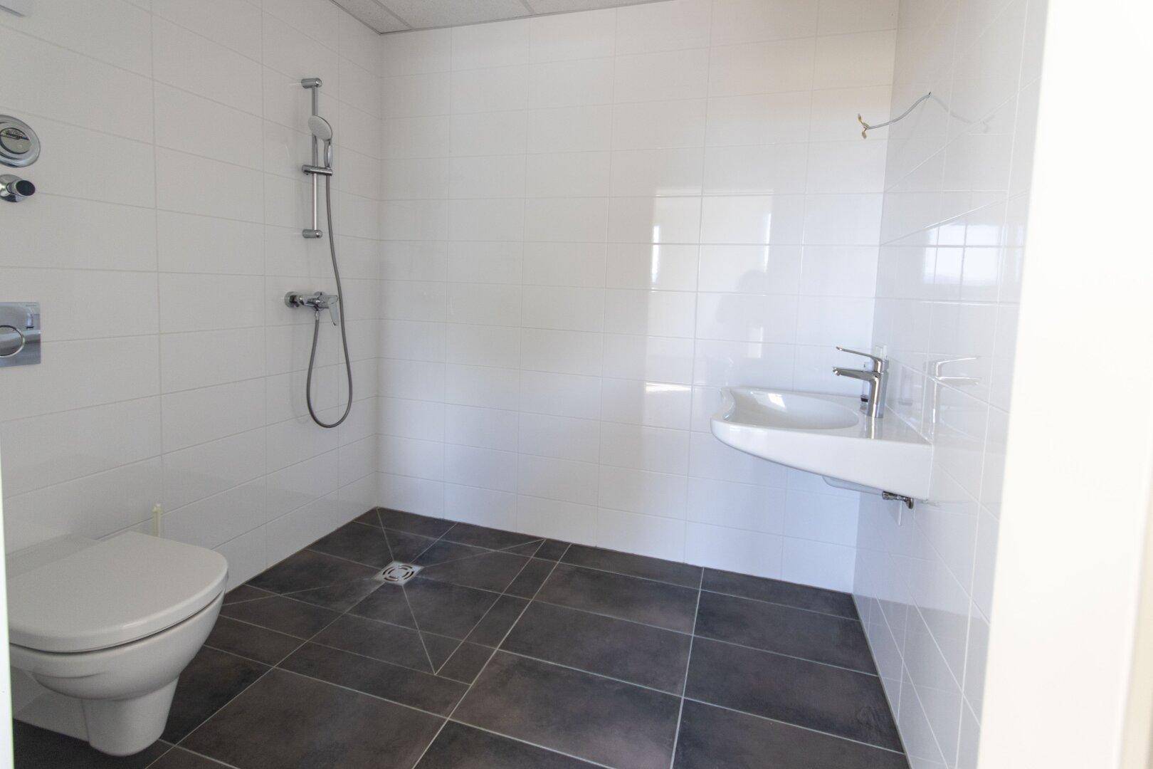 Modernes Badezimmer mit weißen Wandfliesen, dunklem Boden und ebenerdiger Dusche.