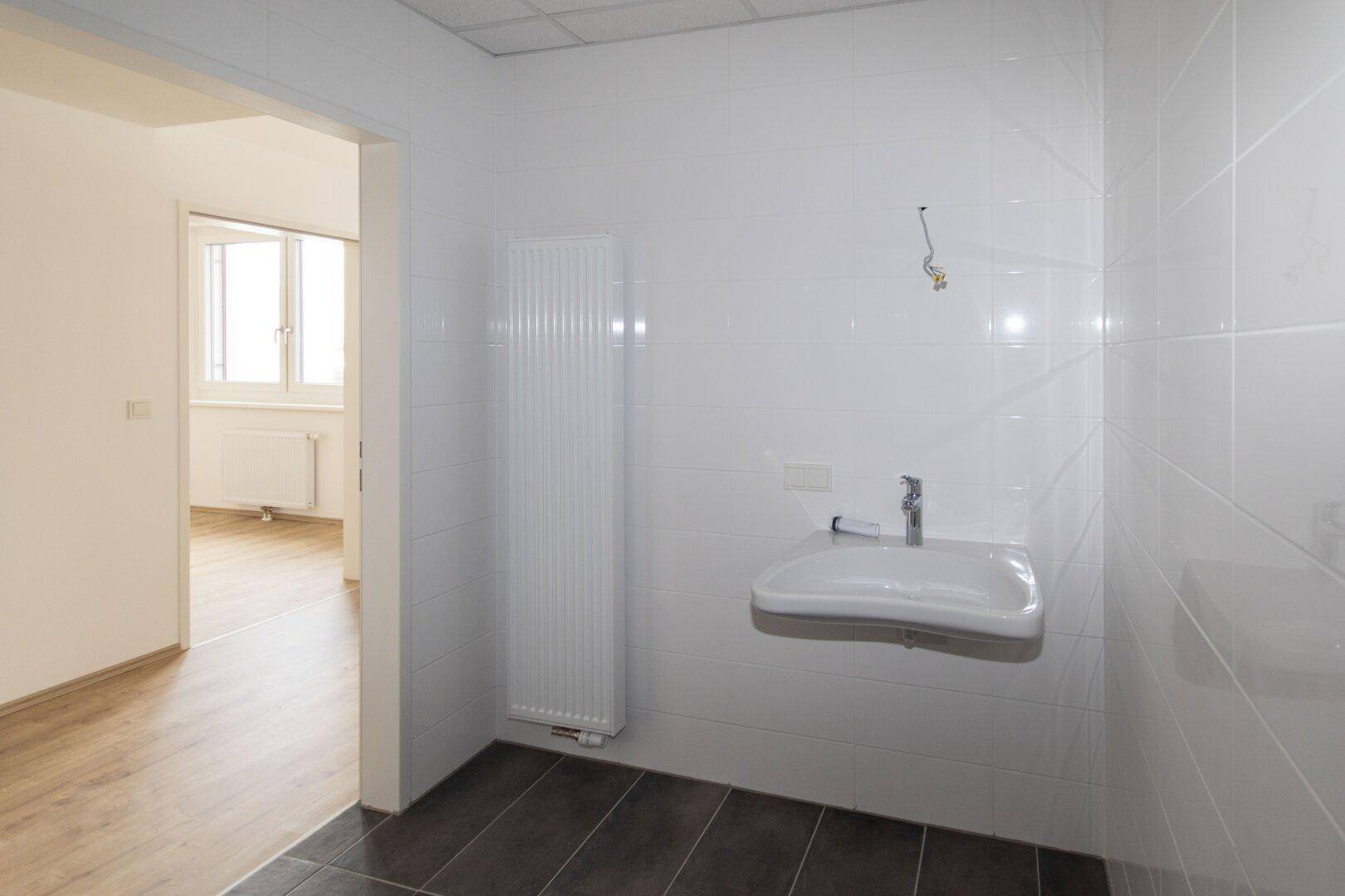 Modern gefliestes WC mit Waschbecken und Heizkörper, bietet Zugang zu einem weiteren Raum.